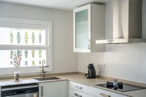 A modern kitchen with a dishwasher, a coffee maker, and a window with decorative glass panels. - House with garden Can Nofre in Playa de Muro (Muro)