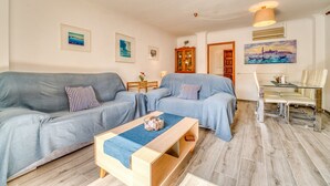 Ein Wohnzimmer mit grauem Sofa, einem Holztisch und einem Glastisch mit Stühlen.