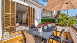 Eine Terrasse im Freien mit Tisch und Stühlen, einem beige farbenen Sonnenschirm und Topfpflanzen.