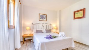 Ein Hotelzimmer mit Bett, Nachttischlampen, einem Nachttisch, einem gerahmten Bild an der Wand und einem Fenster mit Vorhängen.