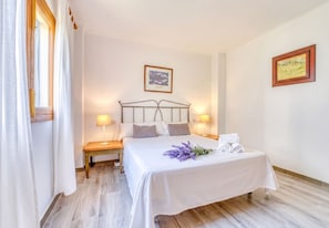 A hotel room with a bed, bedside lamps, a nightstand, a framed picture on the wall, and a window with curtains. - House with garden Can Nofre in Playa de Muro (Muro)