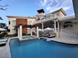 A two-story building with a swimming pool, outdoor seating, and a covered area with umbrellas. - Your Dream Family or Group Getaway: 5 Bedroom Luxury Villa Awaits in Cofresi! (Cofresi)