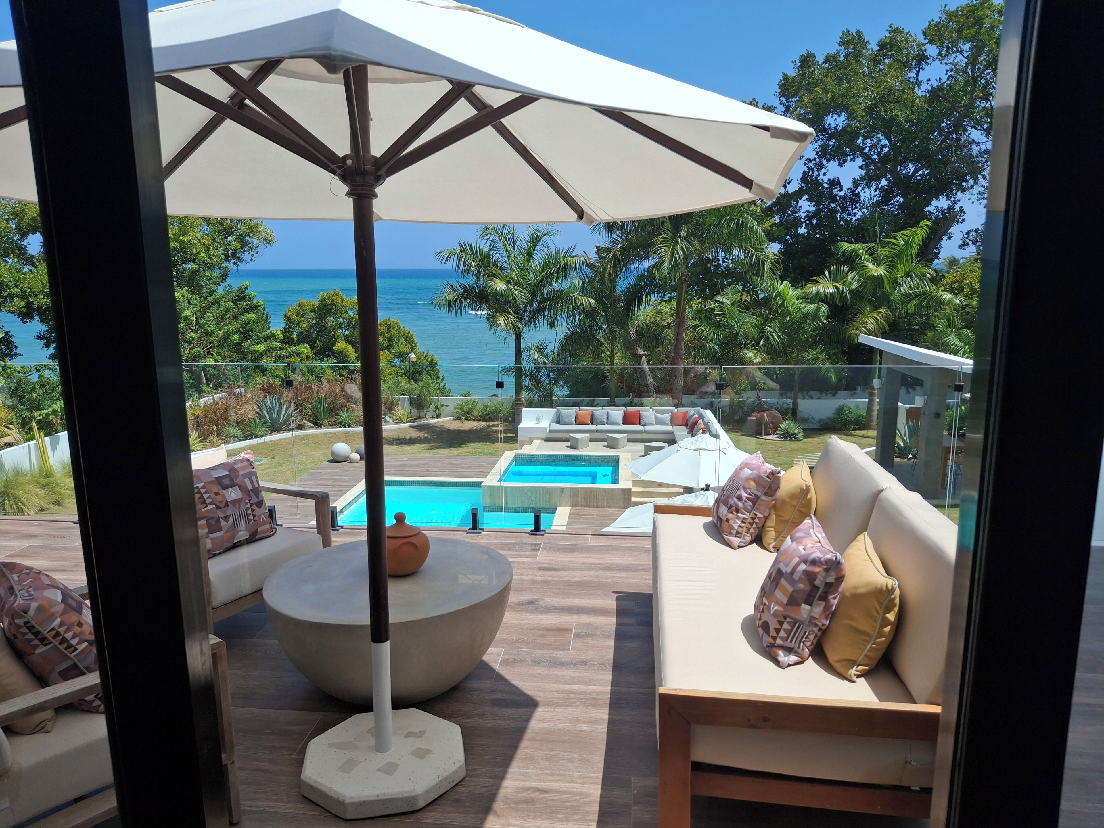 A poolside area with a seating arrangement, a large umbrella, and a view of the ocean.