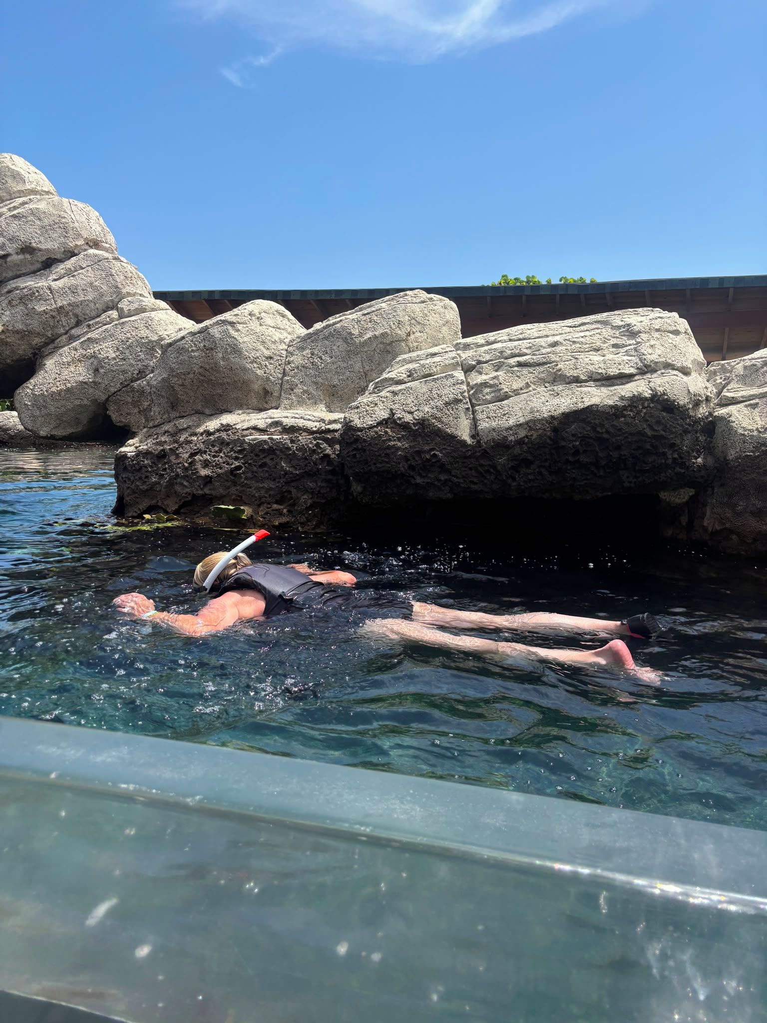 A person swimming in a pool with large rocks and a clear sky.