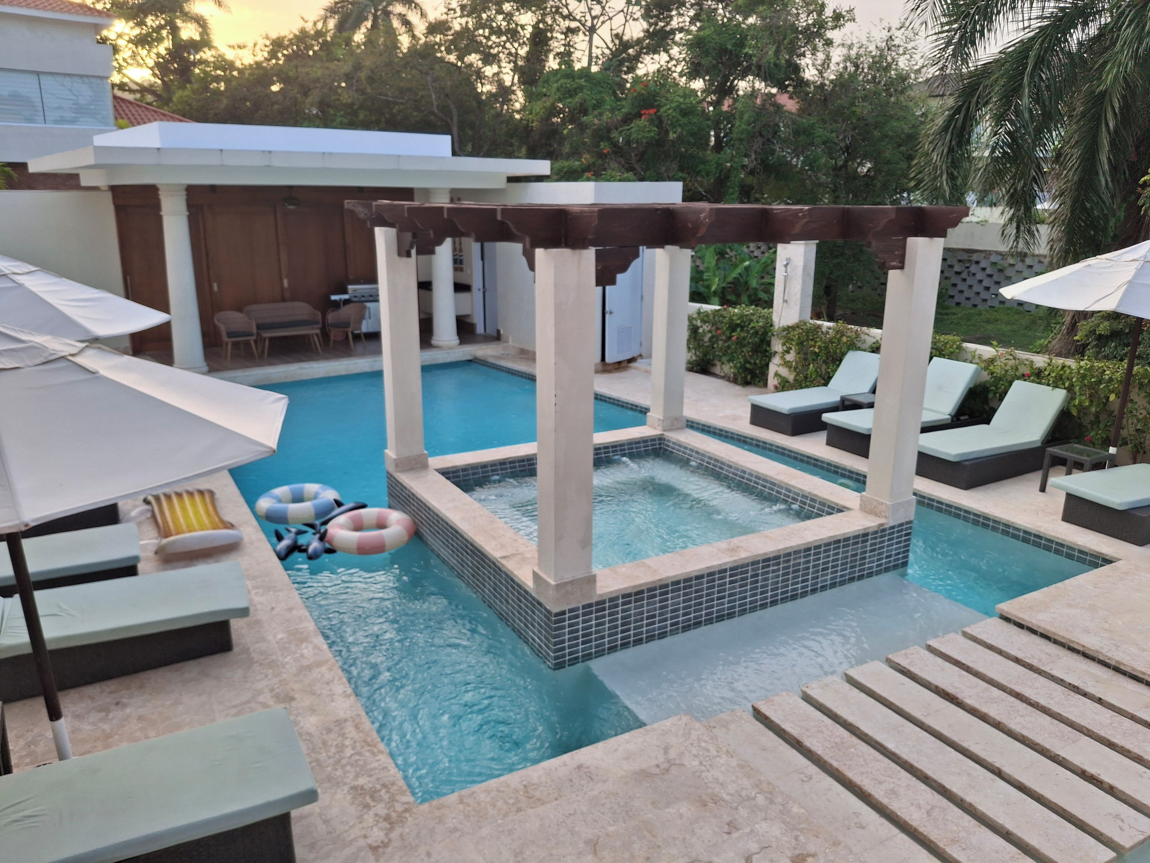 Une piscine avec un jacuzzi, des chaises longues et des parasols.