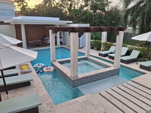 En swimmingpool med jacuzzi, liggestole og parasoller.
