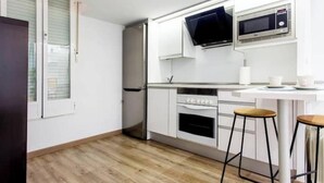 A modern kitchen with white cabinets, a stainless steel refrigerator, a microwave, and two stools. - Industrial-style duplex apartment (Centro)