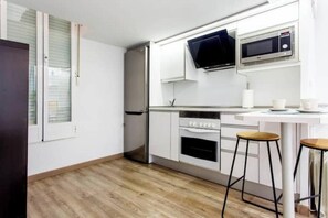 Eine moderne Küche mit weißen Schränken, einem Edelstahlkühlschrank, einer Mikrowelle und zwei Barhocker.