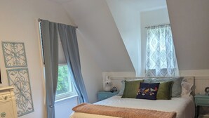 A bedroom with a bed, a dresser, a nightstand, a lamp, and a window with curtains.