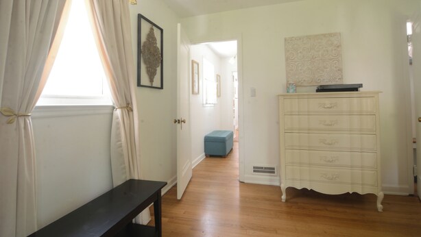 A hallway with a bench, a dresser, and a door leading to another room.