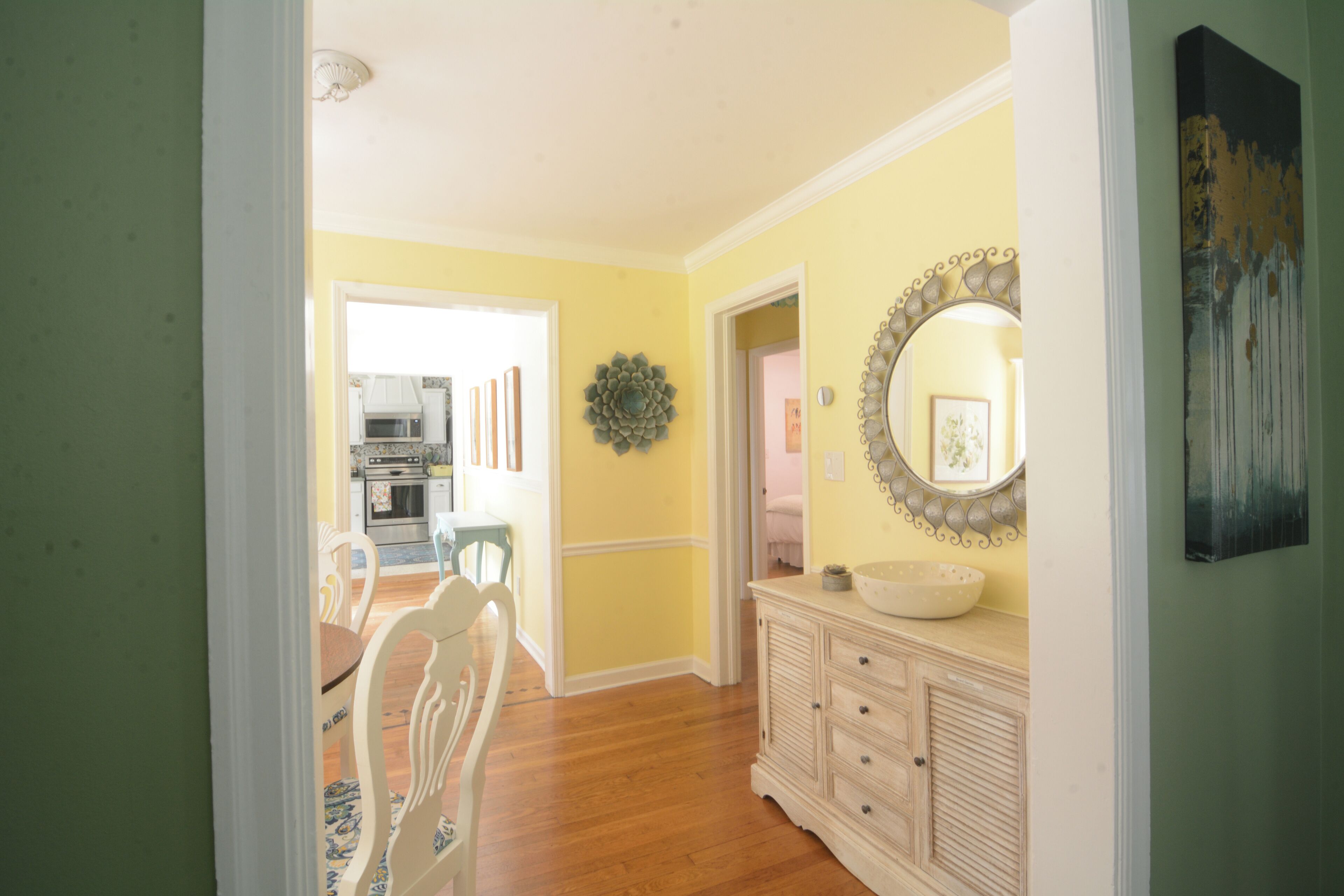 A hallway with a dining area, kitchen, and a decorative mirror.
