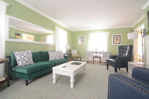 A living room with a green sofa, a white coffee table, a blue armchair, and a fireplace.