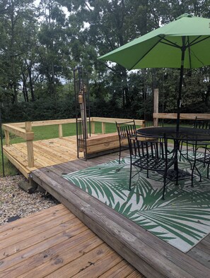 A wooden deck with a table and chairs, surrounded by a wooden fence and greenery.