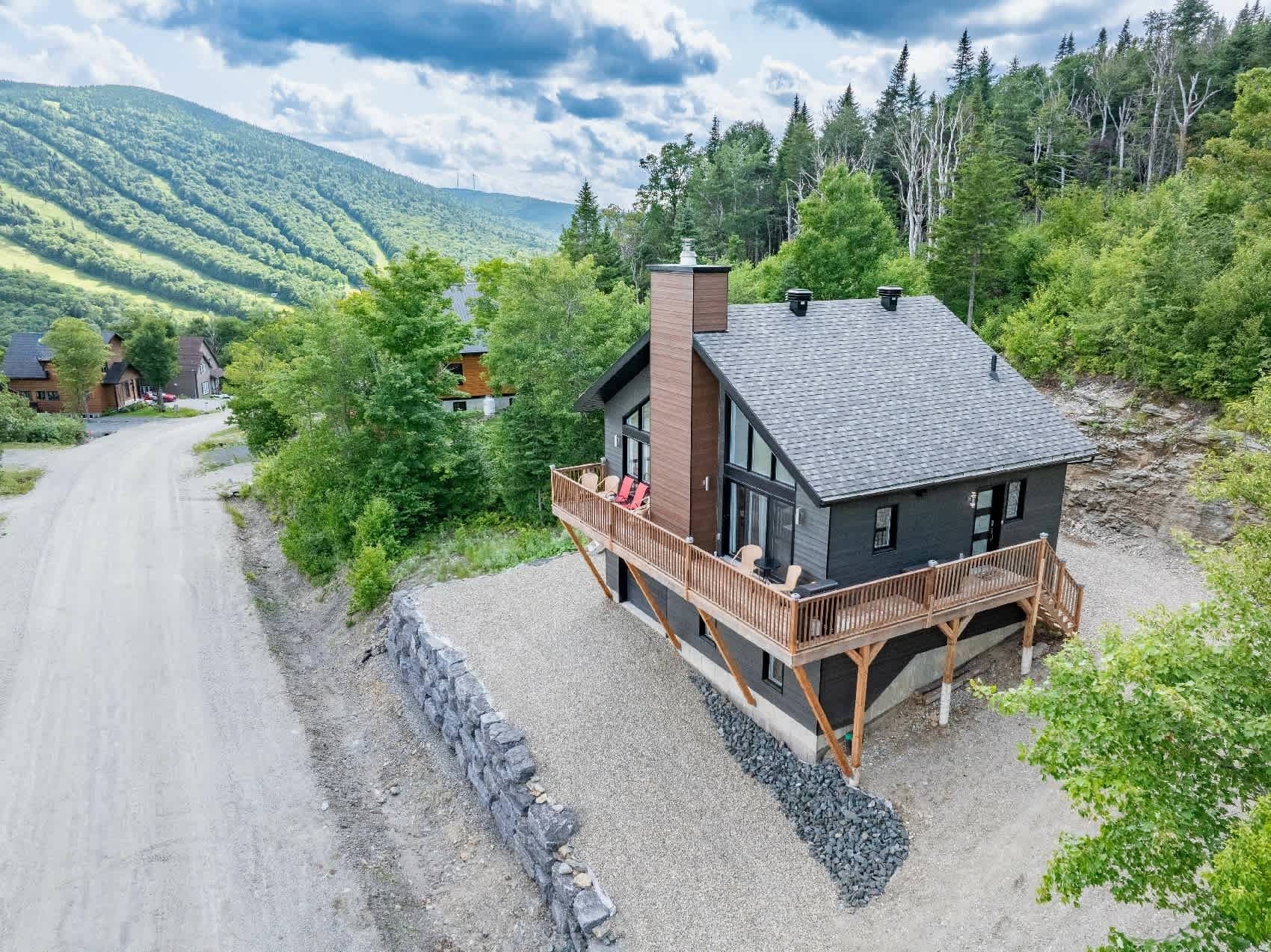 Ein modernes Haus mit Terrasse, umgeben von üppiger Vegetation und Blick auf die Berge.