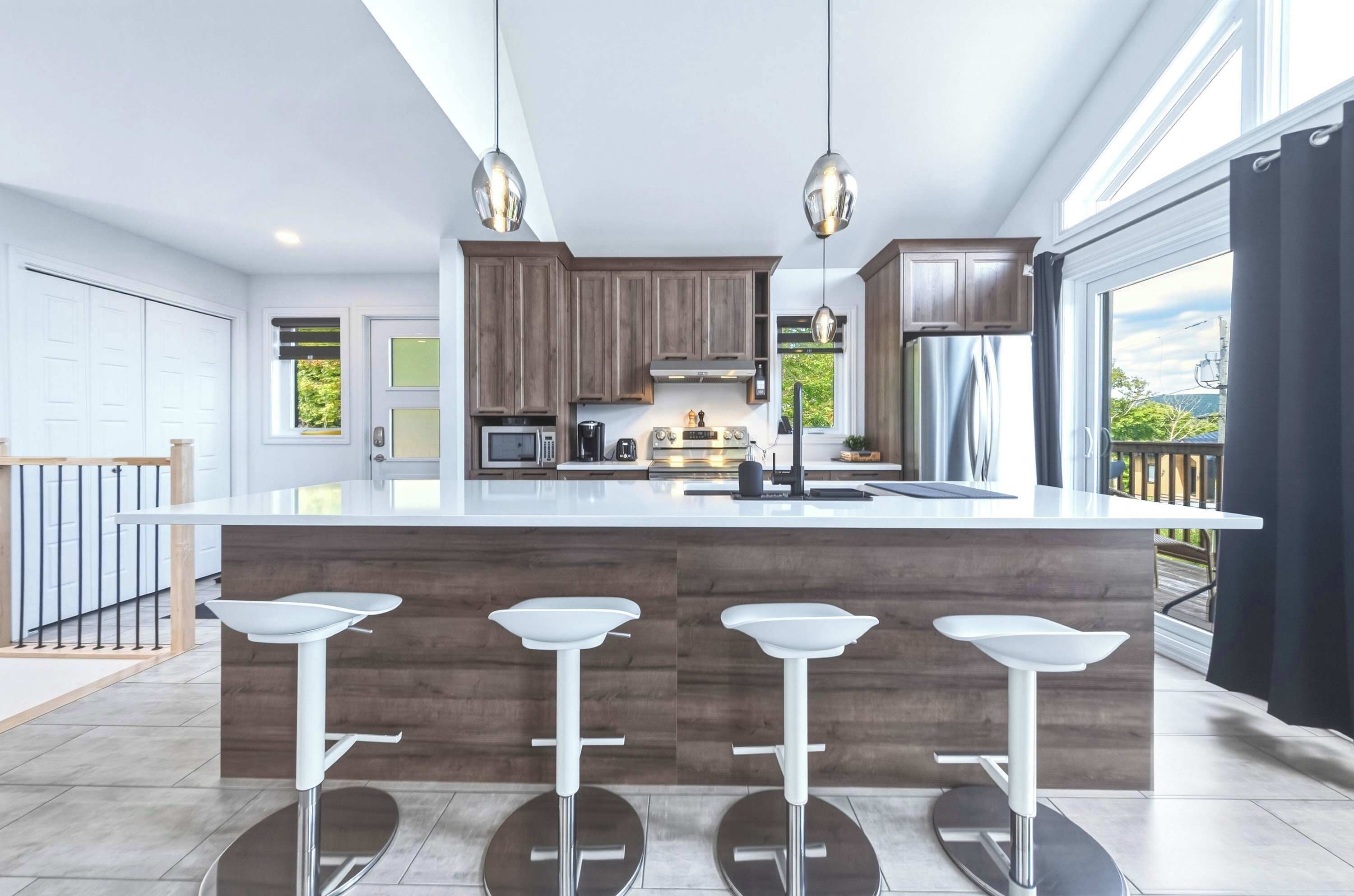Cocina moderna con una isla central, taburetes de bar, armarios de madera e iluminación colgante.