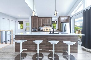 A modern kitchen with a central island, bar stools, wooden cabinets, and pendant lighting. - Spa & Nature | Chalet Le WeSki (Saint-Philémon)