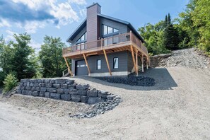 Une maison moderne à deux étages, dotée d’un balcon, d’un mur de soutènement en pierre et d’une allée gravillonnée.