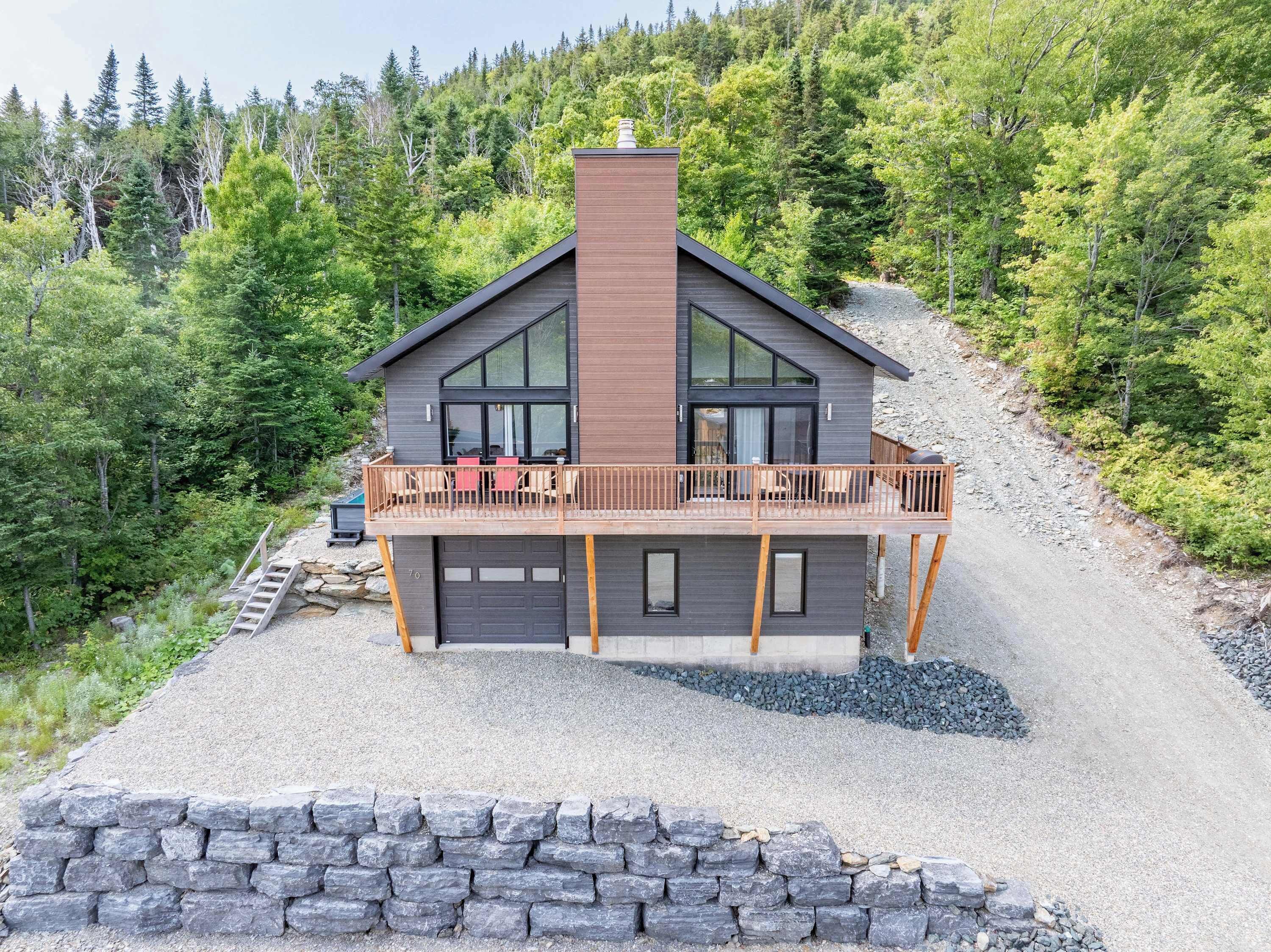 Ein modernes, zweistöckiges Haus mit Balkon, umgeben von bewaldeter Landschaft.