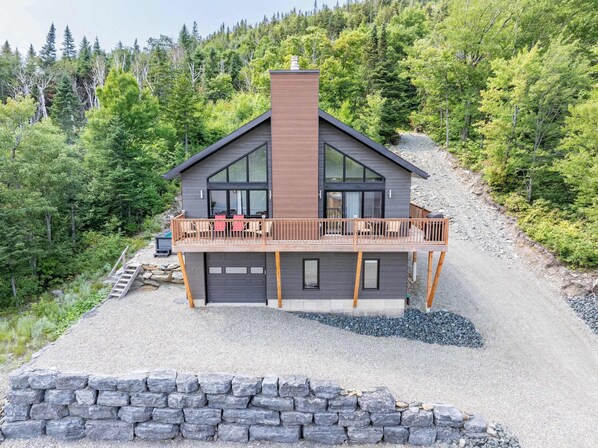 Et moderne hus i to etager med balkon, omgivet af skov.