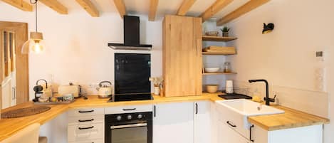 A modern kitchen with wooden beams, a built-in oven, a black range hood, and a white sink.