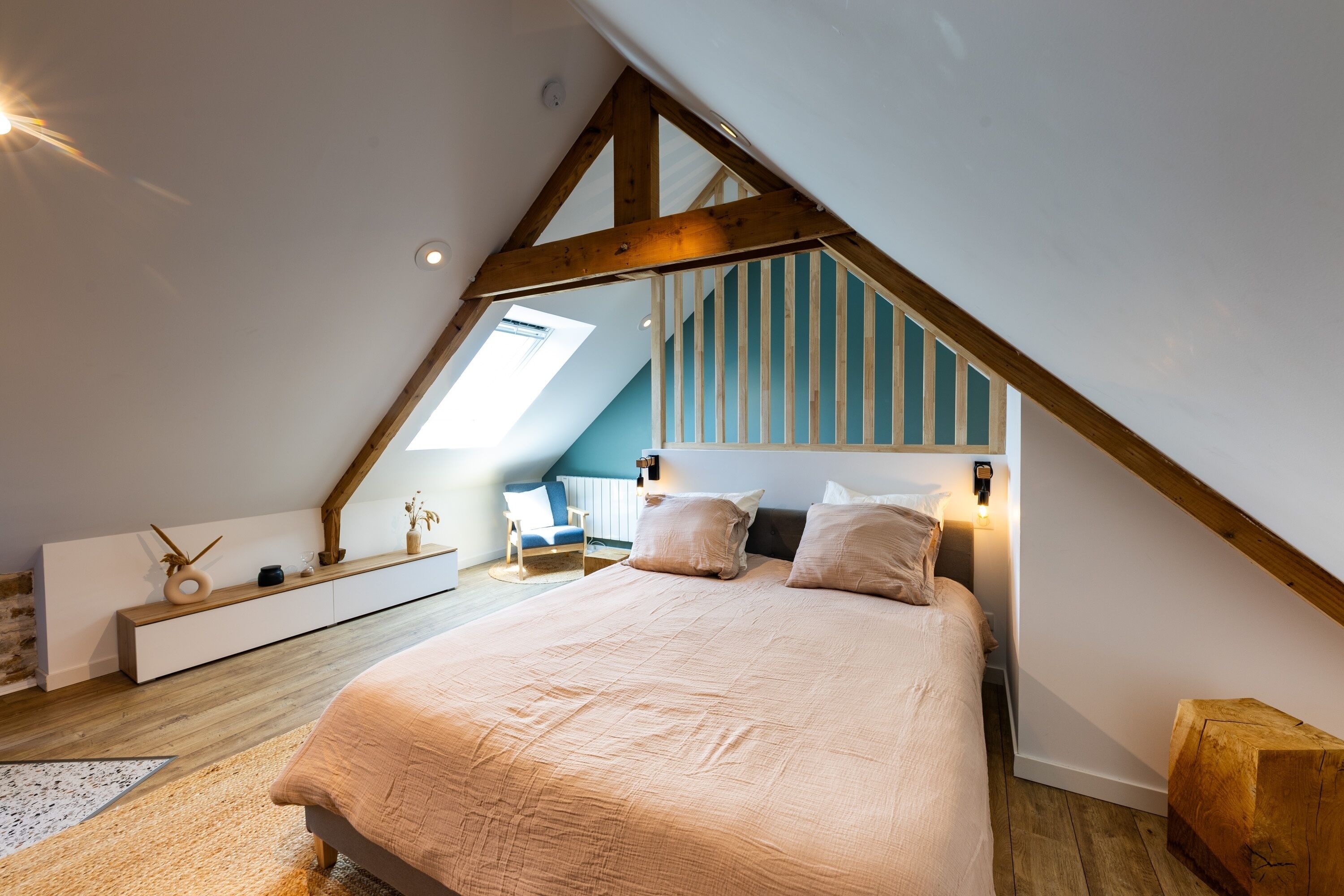 Une chambre à coucher avec un plafond en pente, un lit avec des oreillers, une chaise et une table de chevet agrémentée d’objets décoratifs.