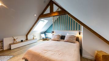 Une chambre à coucher avec un plafond en pente, un lit avec des oreillers, une chaise et une table de chevet agrémentée d’objets décoratifs.
