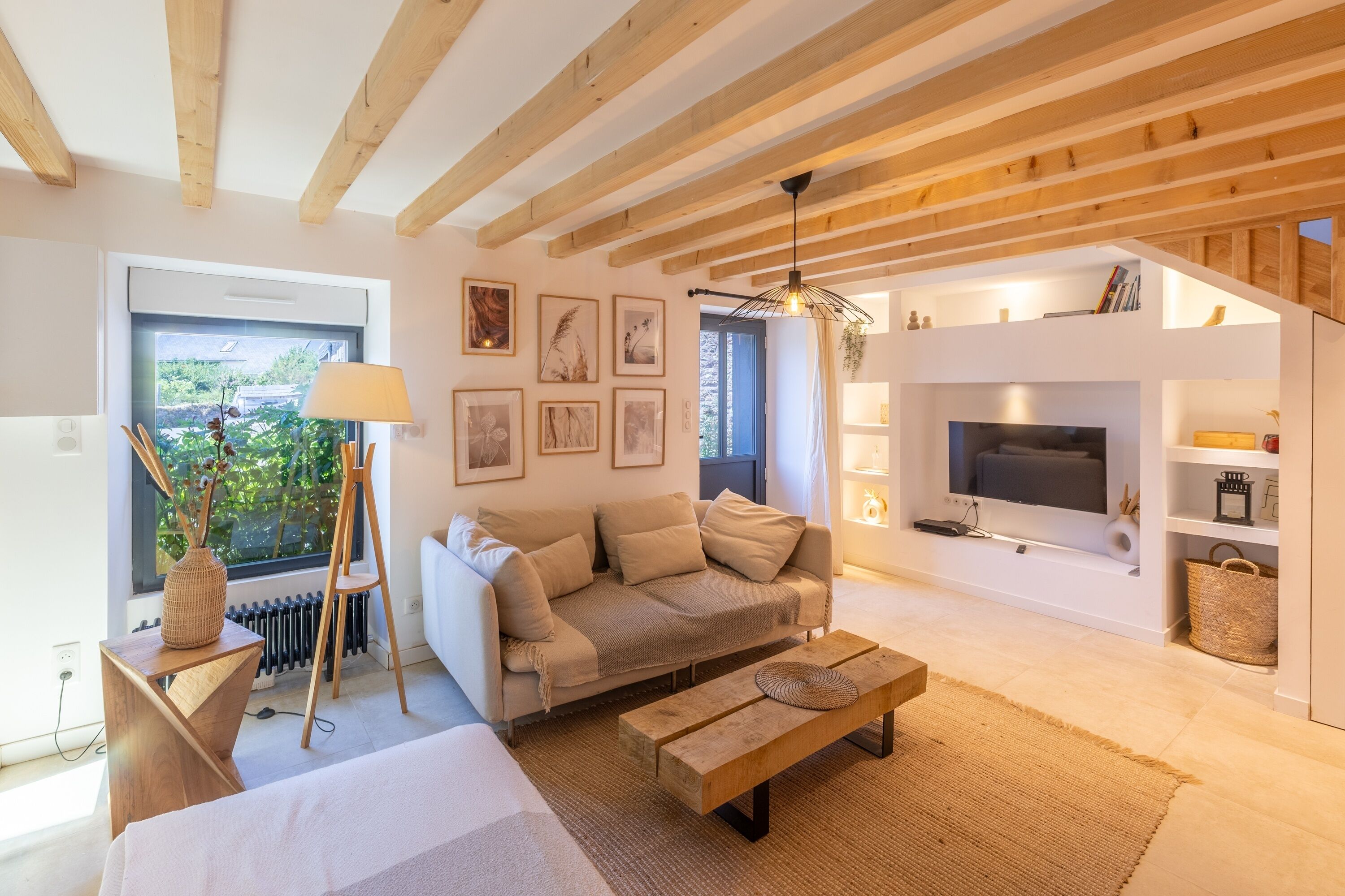 Una sala de estar moderna con un sofá, una mesa de centro y un televisor. Se ve un ventanal con vistas a áreas verdes.