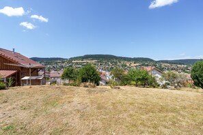 Ein Wohngebiet mit Häusern, ein Holzhaus mit rotem Dach und eine hügelige Landschaft im Hintergrund.