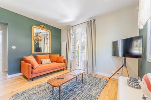 A living room with a sofa, a coffee table, a television on a stand, and a large mirror. - Villa de la Hève - Rénovée, 700 m de la plage (Ouistreham)