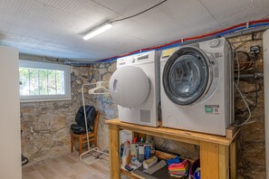 Un cuarto de lavandería con dos lavadoras, un tendedero y un estante de madera con productos de limpieza.
