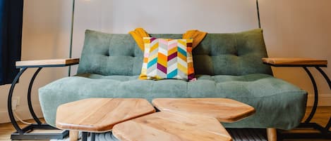 A green sofa with a colorful chevron pillow, two wooden side tables, and two floor lamps.