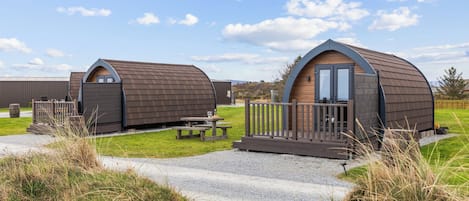 Two small, curved-roofed cabins with a wooden deck and a picnic table in between.