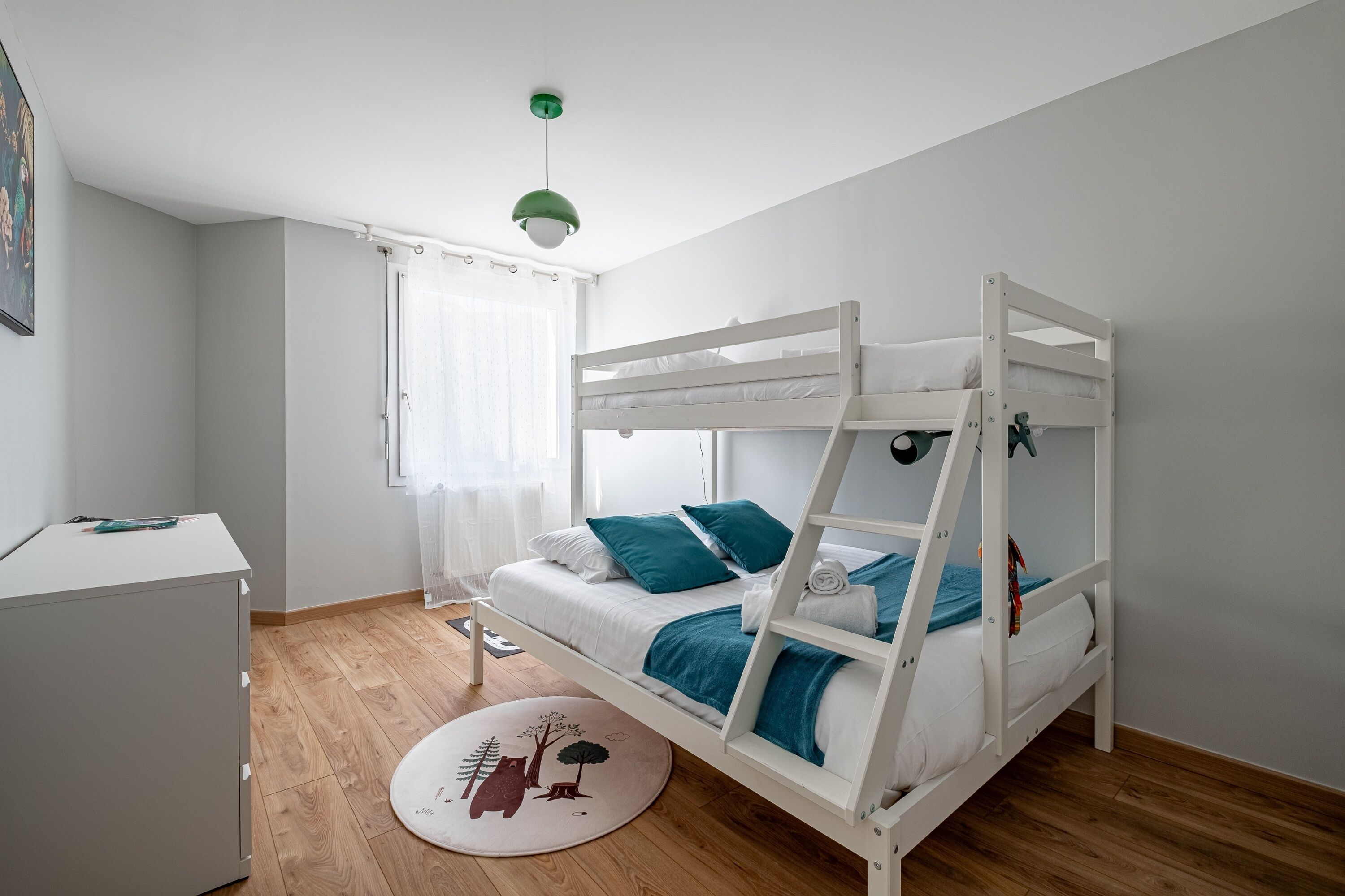 A bunk bed room with a desk, a window with curtains, and a round rug with a tree design.