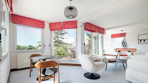 Ein modernes Wohnzimmer mit Essbereich, großen Fenstern mit roten Vorhängen, einem weißen Sofa und einer Gitarre an der Wand.