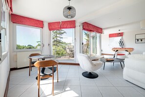 Ein modernes Wohnzimmer mit Essbereich, großen Fenstern mit roten Vorhängen, einem weißen Sofa und einer Gitarre an der Wand.