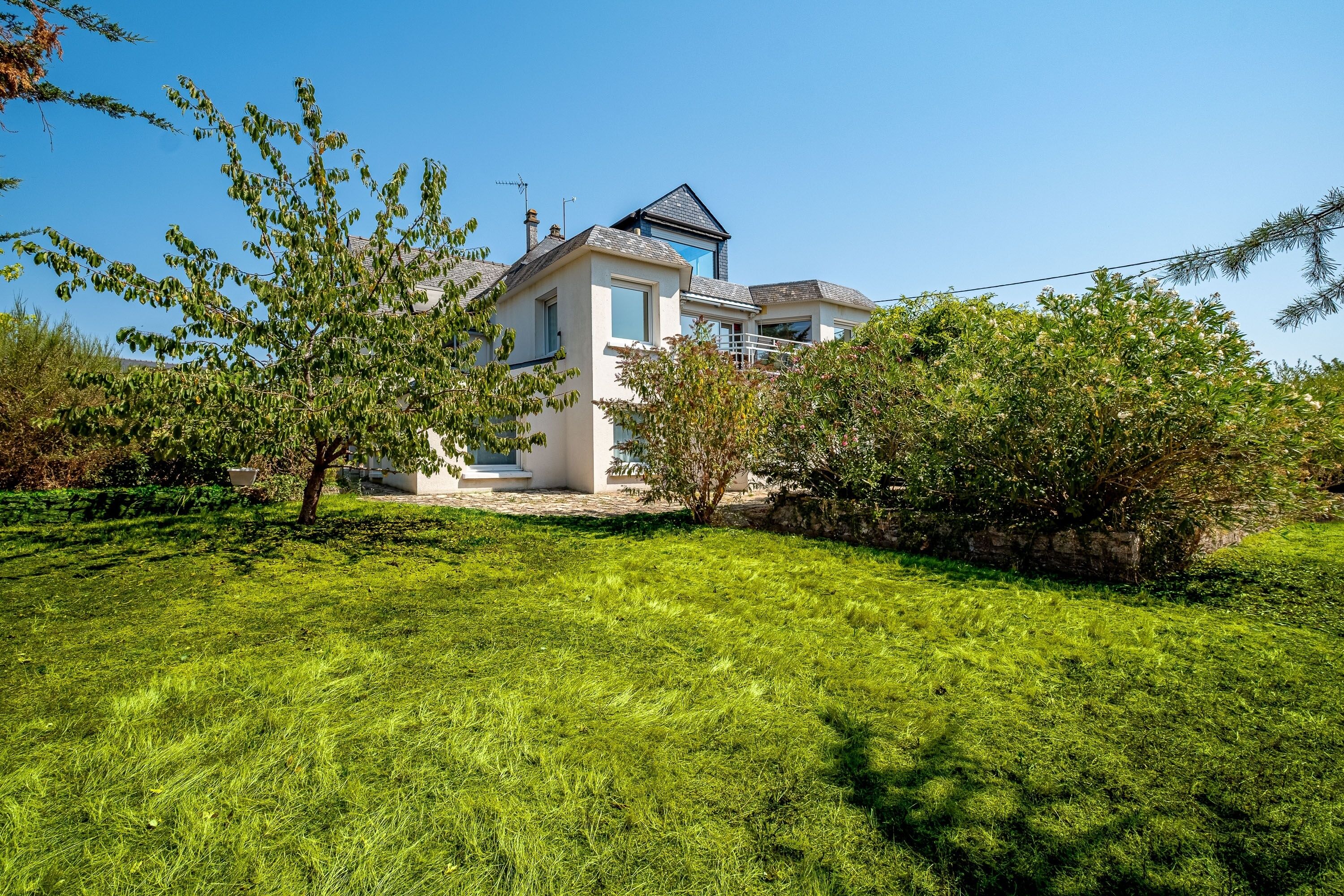 A two-story house with a well-maintained lawn and a stone wall.