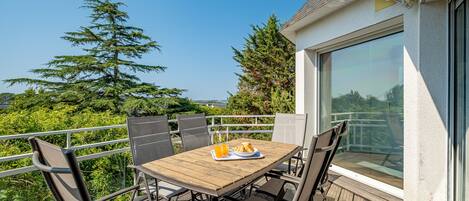 Une terrasse en bois avec une table et des chaises, offrant une vue panoramique sur un paysage verdoyant avec des arbres et un ciel dégagé.