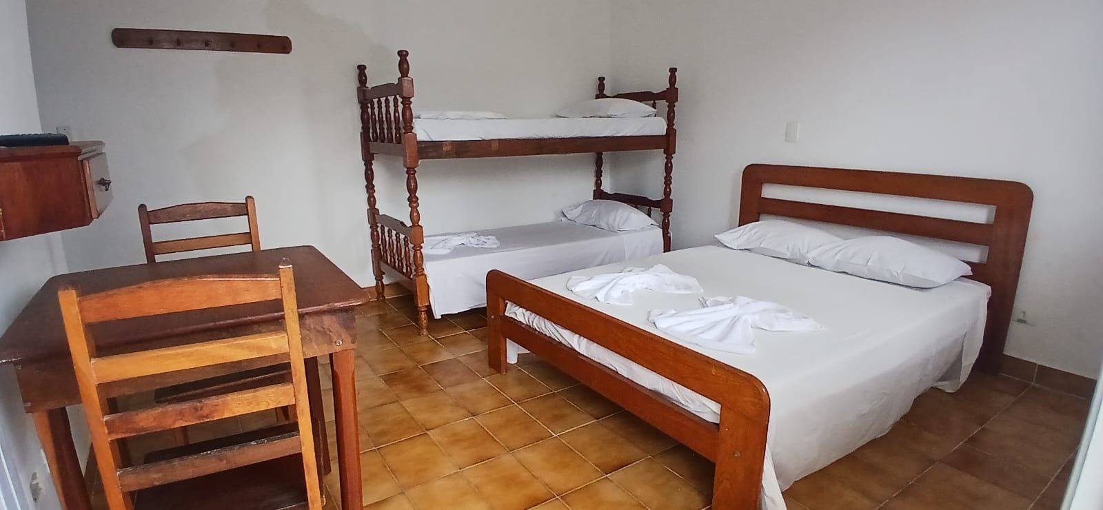 Una habitación con una cama individual, una litera, una silla de madera y una pequeña mesa.