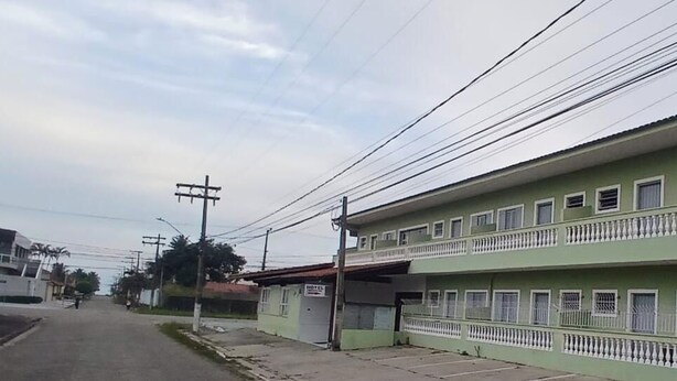 Un edificio de dos pisos con varias ventanas y balcones, un área de estacionamiento al frente y líneas eléctricas aéreas.