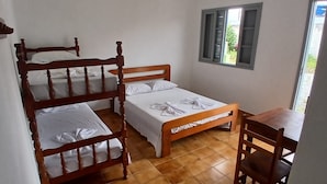 Un dormitorio con dos literas de madera, una cama individual, una mesa de madera y una ventana con contraventanas.