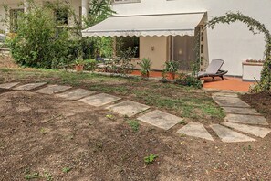 A garden area with a paved pathway leading to a covered seating area with a chair. - LuisHome - Imperia: apartment in villa (Imperia)