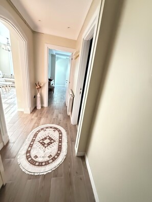 A hallway with a patterned rug, wooden flooring, and a door leading to another room.