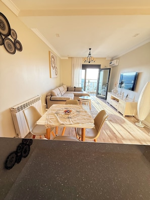 A modern living room with a dining area, a sofa set, a TV, and a balcony with a view.