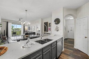 A modern kitchen with a central island, a dining area with a view, and a hallway leading to a door. - Penthouse w/ Lake View | Free Resort Access | Disney 9 min (Four Corners)