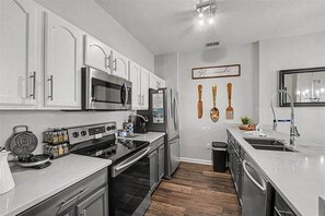 A modern kitchen with white cabinets, stainless steel appliances, and a wooden floor. - Penthouse w/ Lake View | Free Resort Access | Disney 9 min (Four Corners)