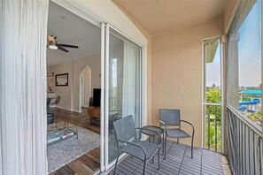 Un balcon avec vue sur un parc aquatique, une porte-fenêtre coulissante donnant sur un espace de vie équipé d’un téléviseur, et deux fauteuils.