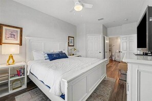 A bedroom with a large bed, a bedside table with a lamp, a bookshelf, and a door leading to a bathroom. - Penthouse w/ Lake View | Free Resort Access | Disney 9 min (Four Corners)
