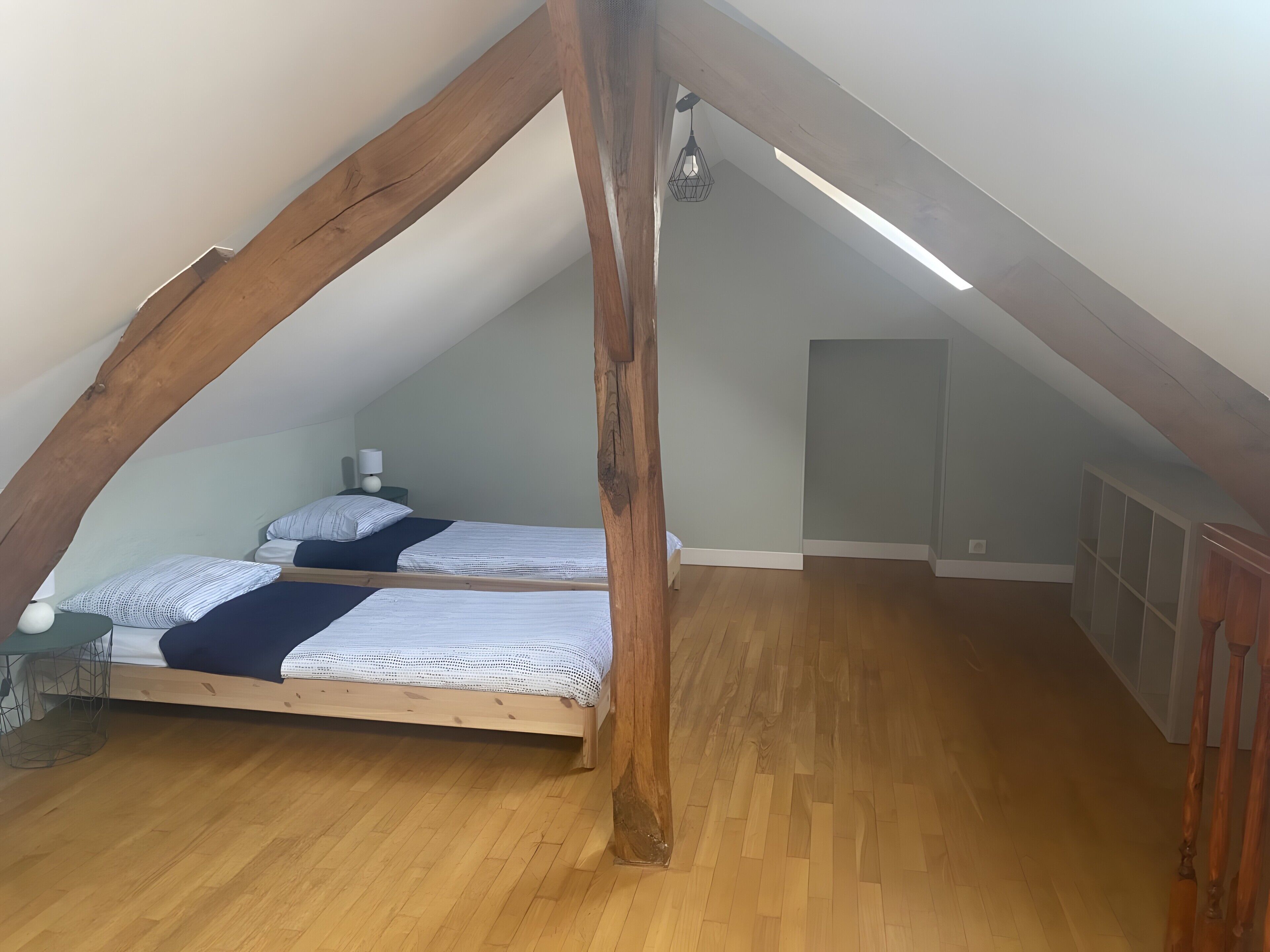 Un dormitorio tipo loft con dos camas, vigas de madera, una lámpara colgante y suelo de madera.
