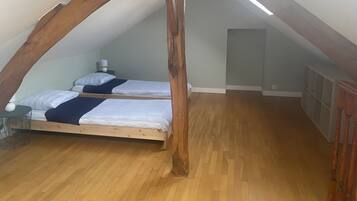Un dormitorio tipo loft con dos camas, vigas de madera, una lámpara colgante y suelo de madera.