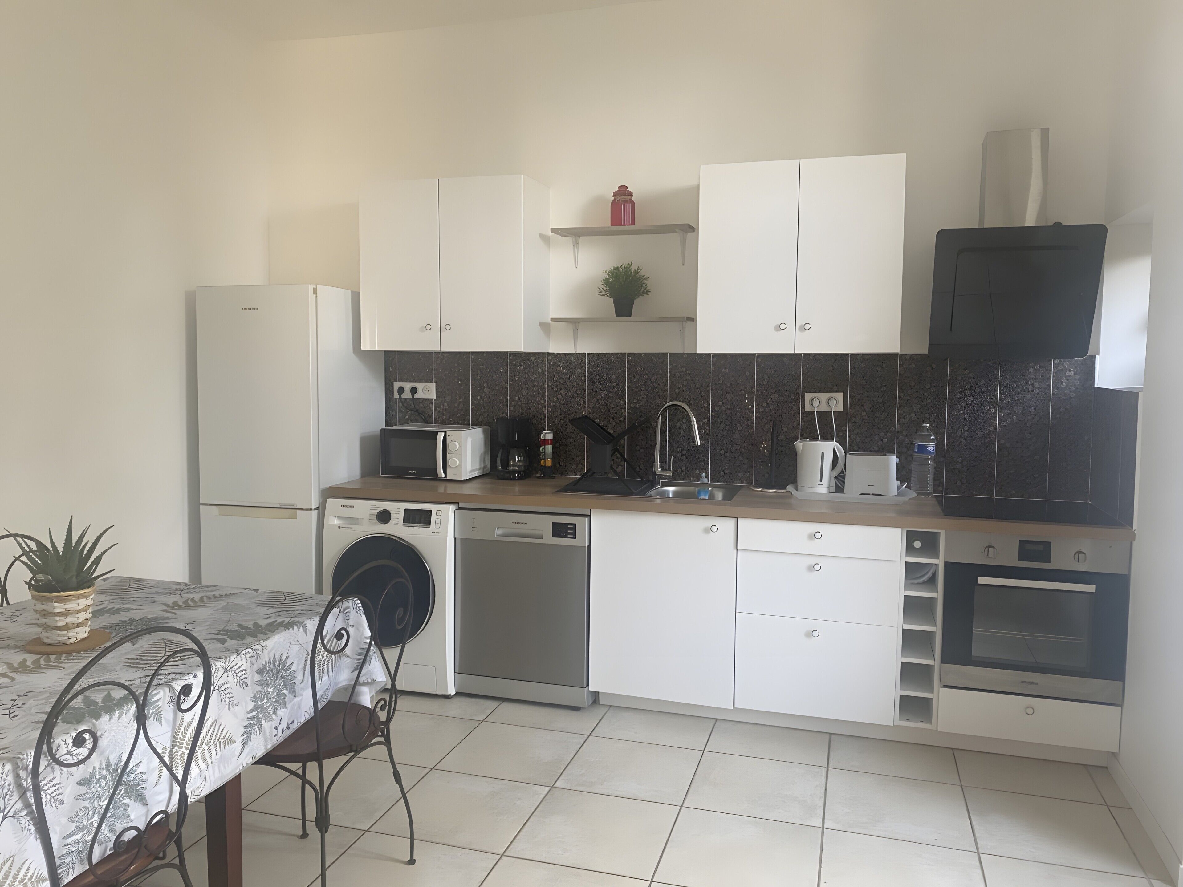 Una cocina compacta con gabinetes blancos, microondas, cafetera y lavavajillas.
